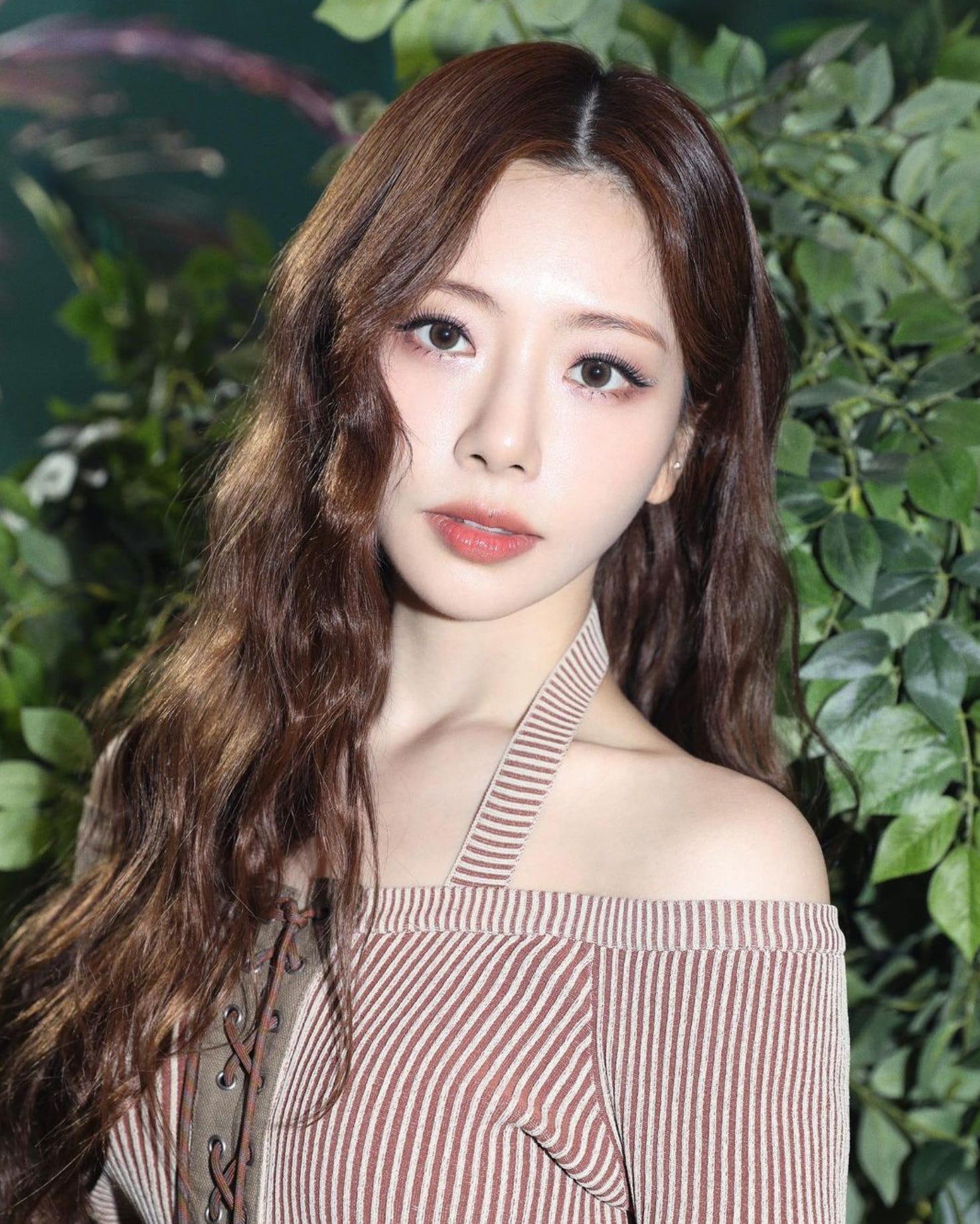 Dreamcatcher's JiU, with brown hair, striped top, with green leaves in the background.