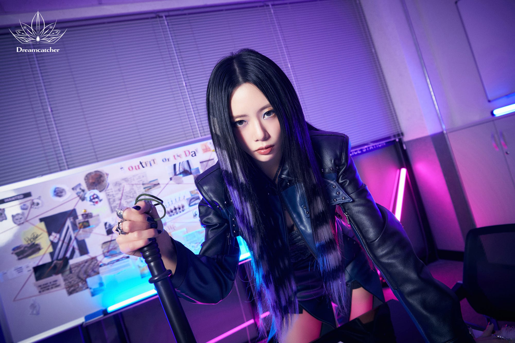 Dreamcatcher's JiU poses staring intently into the camera, with a police baton in her hand, a board connecting together elements from a case in an office setting.