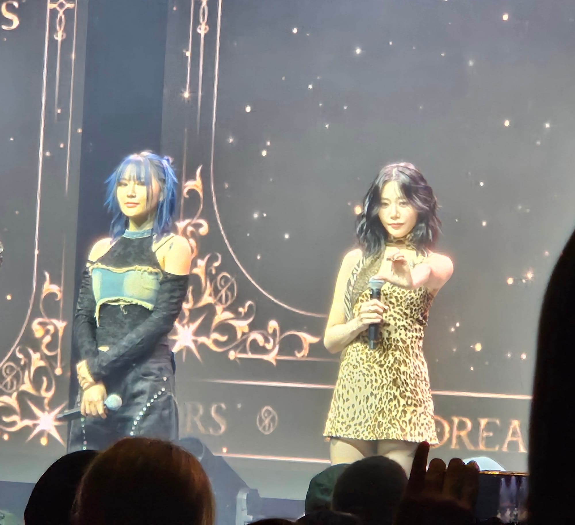 Siyeon looks into the crowd as JiU extends her arm to fans making a half heart.