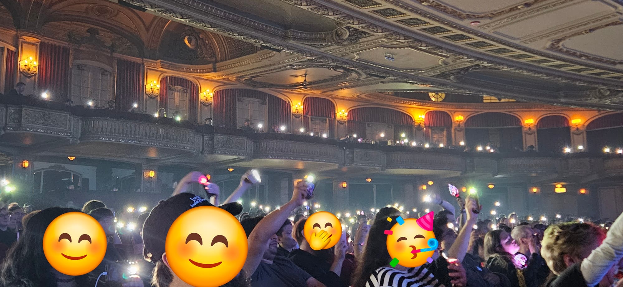 Audience shot at the Chicago Theatre Dreamcatcher show, with recognizable faces censored and flashlights on phones out.