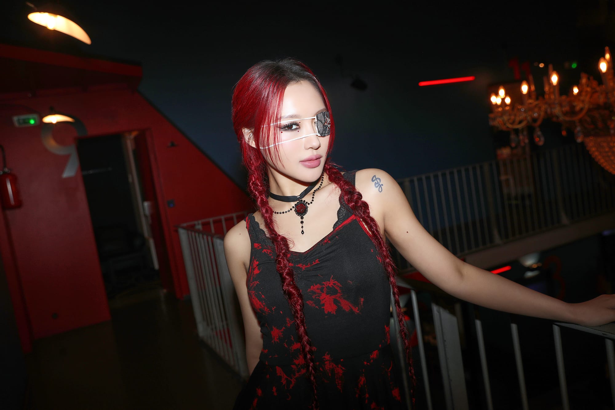 Siyeon takes a picture with red hair and red and black outfit with a protective patch over one eye.