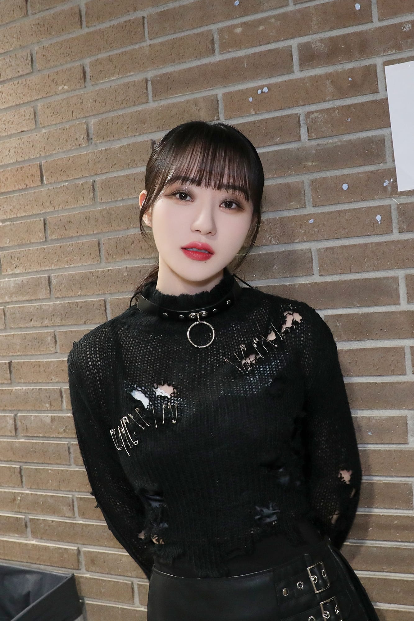 SuA, dressed in black, takes a picture against a brick wall.