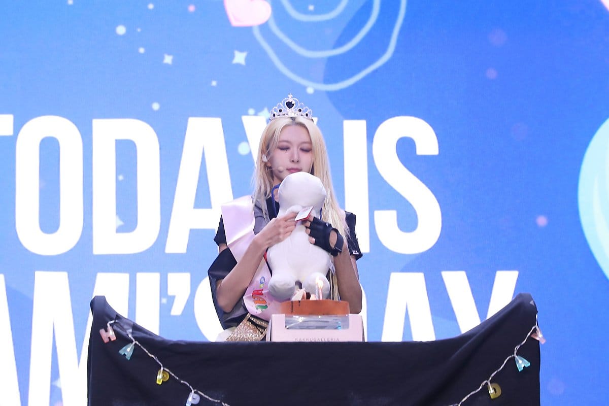 Dami closes her eyes to make a wish while holding a doll in front of a birthday cake.