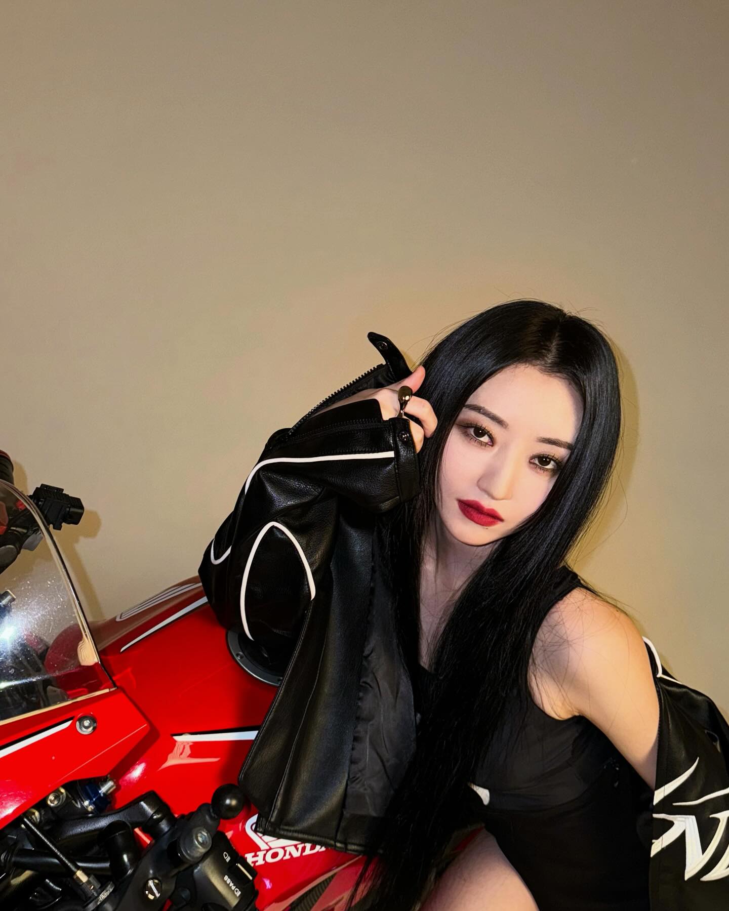 SuA wearing black posing for the camera with a red Honda motorcycle.