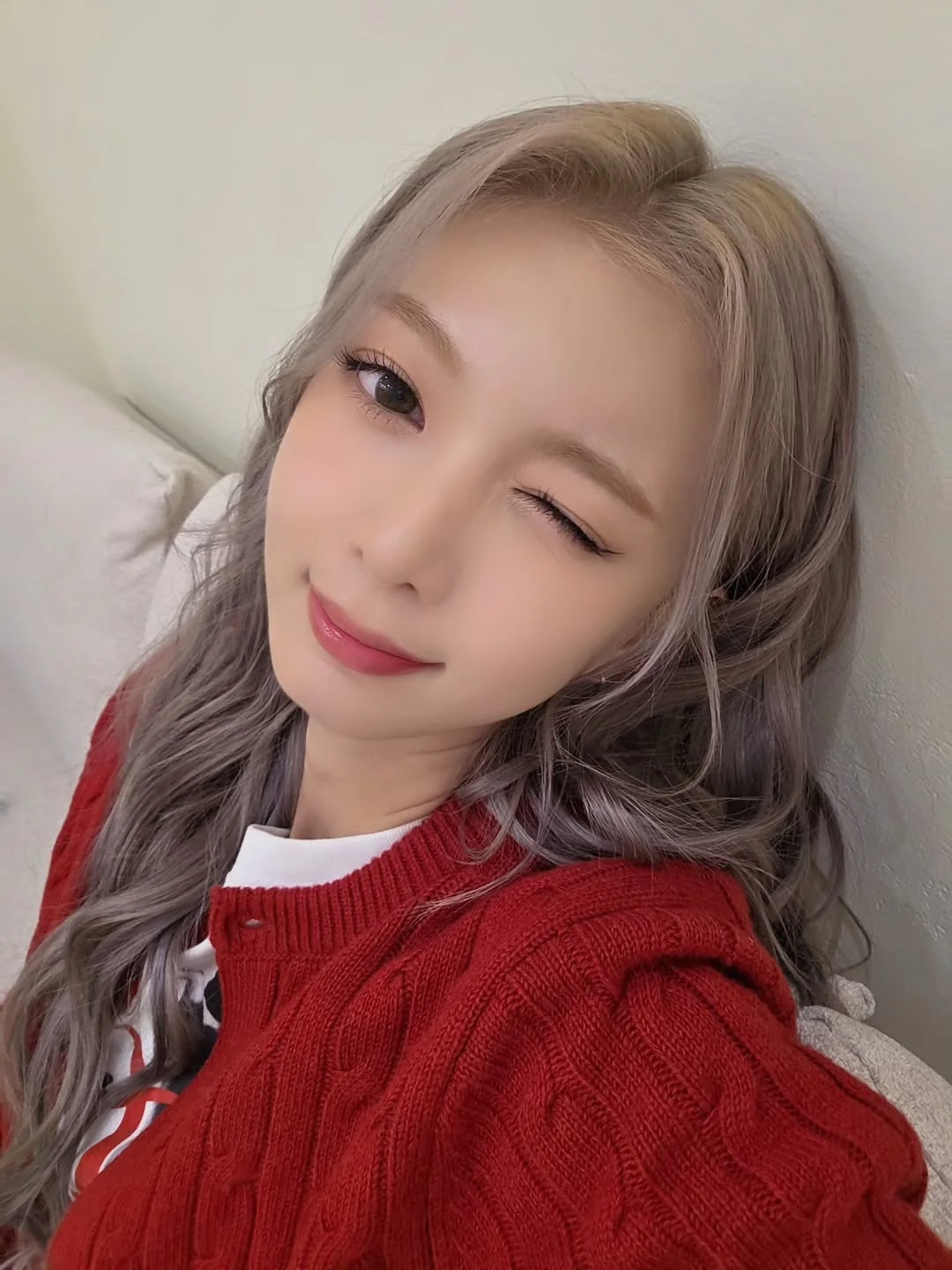Dami winking and smiling for the camera while in a red sweater.
