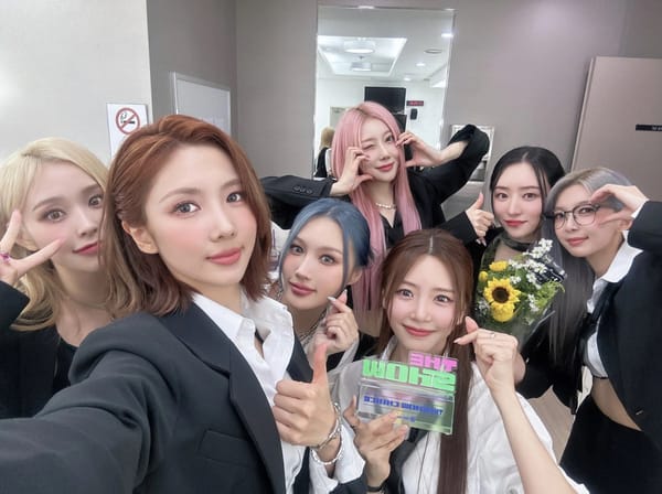 K-Pop girl group Dreamcatcher posing for a group selfie dressed in black and white suits with SBS MTV The Show's trophy.