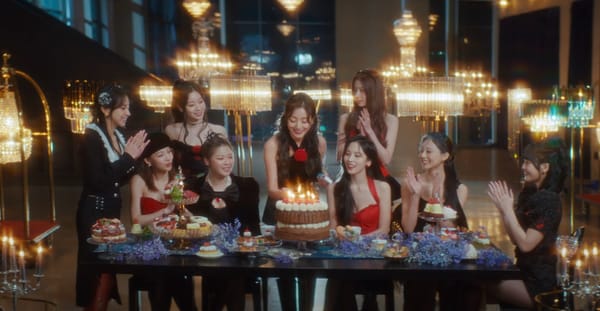 Members of TWICE gather around a table with sweets and a birthday cake with 10 candles.