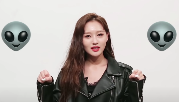 Siyeon in a black leather jacket and brown hair on a white background talking to fans with alien icons on either side