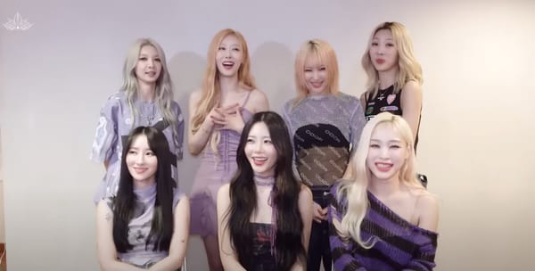 Dreamcatcher, dressed in concert clothes, smiling and talking sitting against a beige background.