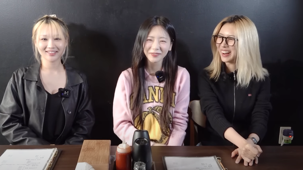 JiU (in pink), Siyeon (in leather jacket) and Yoohyeon (in glasses) smile while greeting fans while filming in a restaurant.