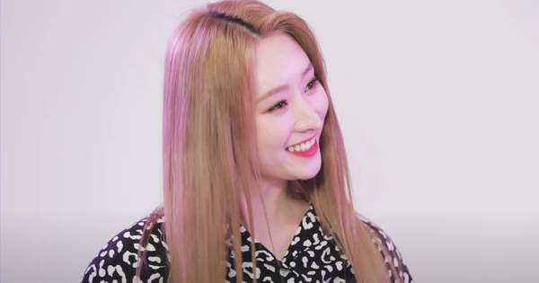 SuA in blonde hair and a black and white blouse looking towards Handong while smiling.