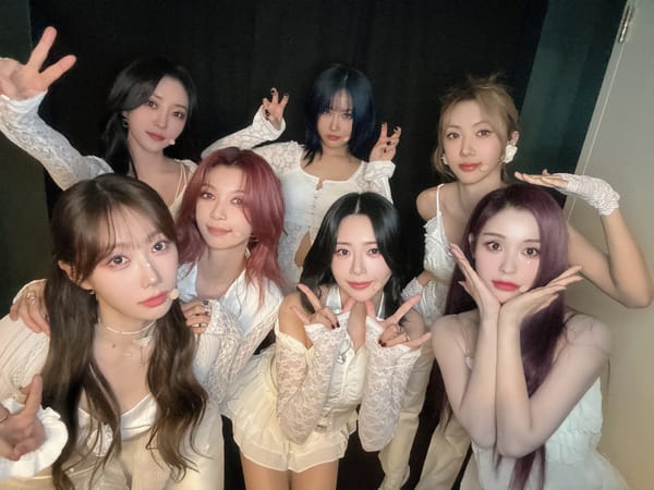 Dreamcatcher, in white outfits, smiling for the camera in New York City.