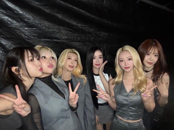 Dreamcatcher, without Handong, smiles for the camera against a black background wearing grey.