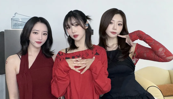 SuA, Yoohyeon, and JiU are dressed in red and black and smile/pose for the camera.